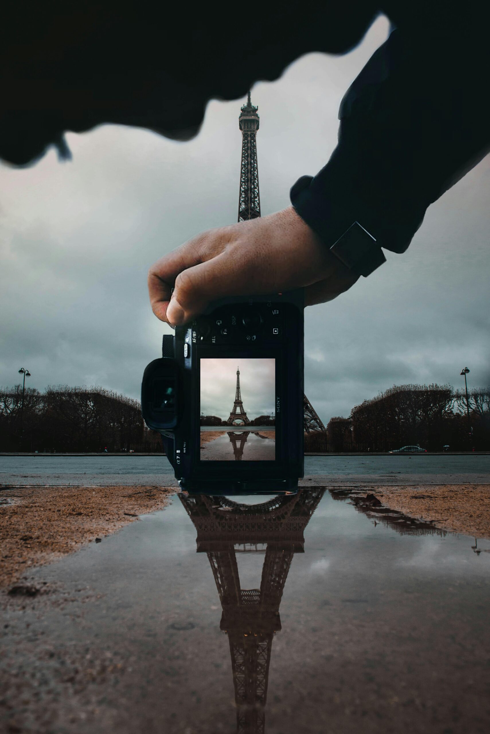 A unique perspective of the Eiffel Tower reflected in a puddle through a camera viewfinder.